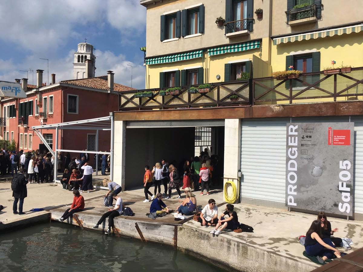 An image of people sitting outside the Scotland + Venice venue in Venice, alongside a canal