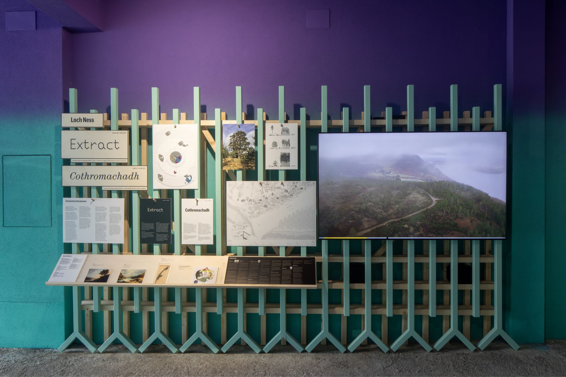 A photograph of a section of an exhibition, featuring boards of text and images and a screen showing videos of the Loch Ness landscape.